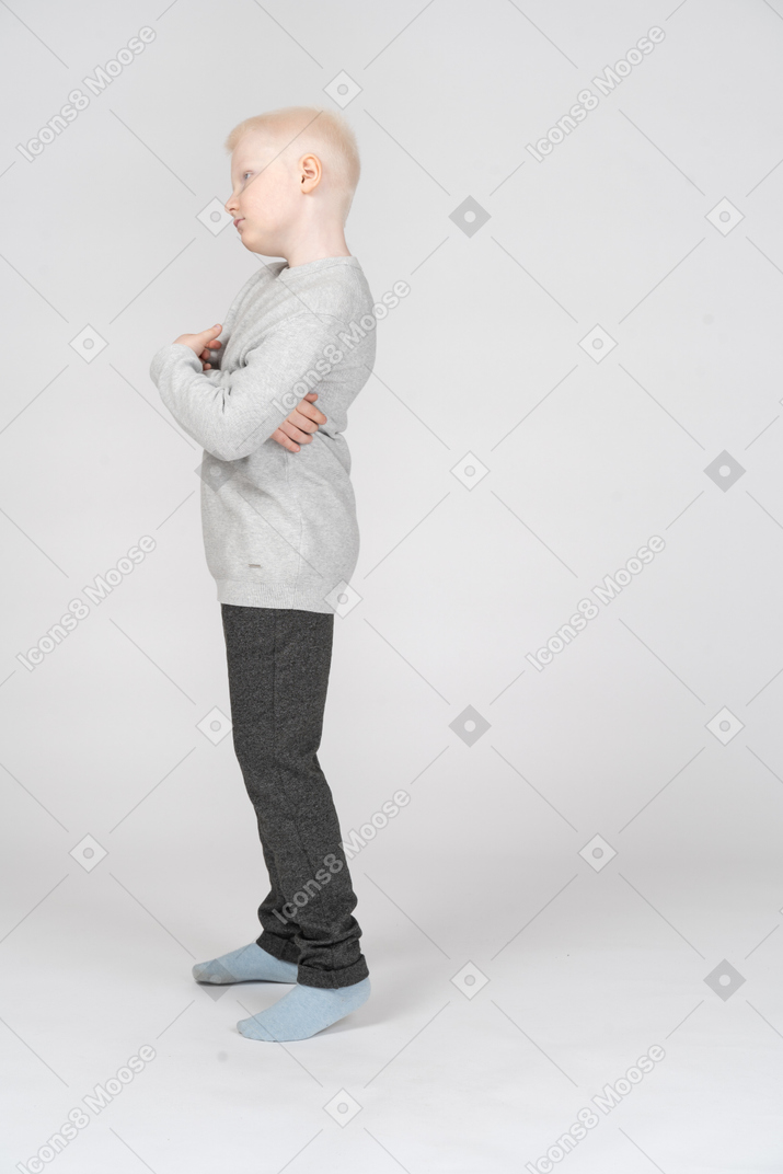 Side view of a  naughty kid boy tilting head while crossing hands