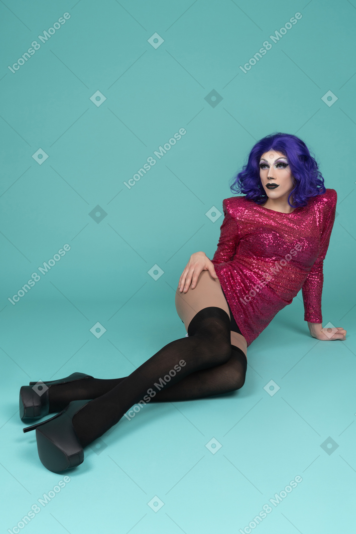 Drag queen in pink sequin dress sitting on the ground with legs stretched out