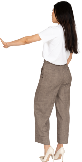 Vista posteriore di tre quarti di una giovane donna in calzoni che tende la mano