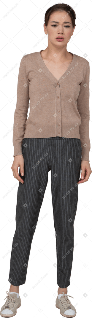 プルオーバーでじっと立っている困惑した若い女性とまっすぐに見えるズボンの正面図