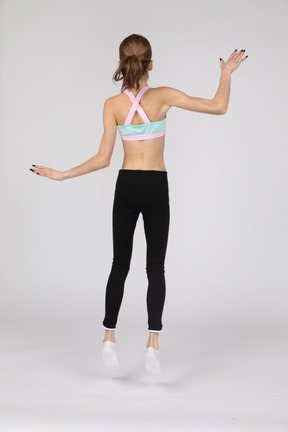 Vista traseira de uma adolescente em roupas esportivas pulando e acenando com a mão
