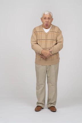 Front view of an old man in casual clothes showing tongue