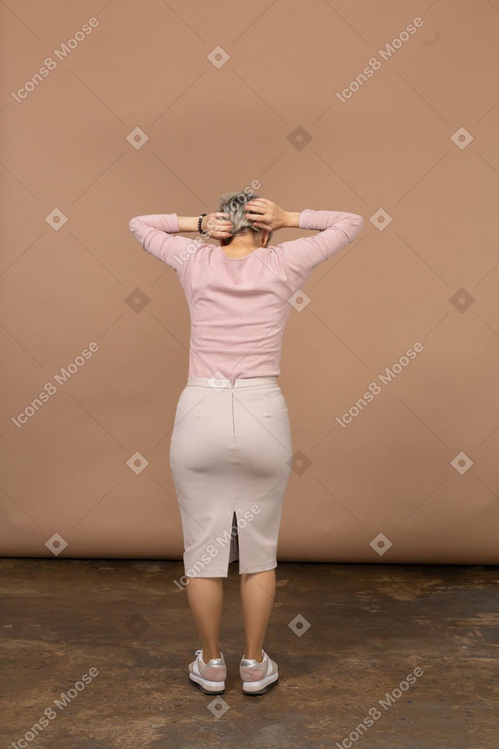 Vista posteriore di una donna in abiti casual in piedi con le mani dietro la testa