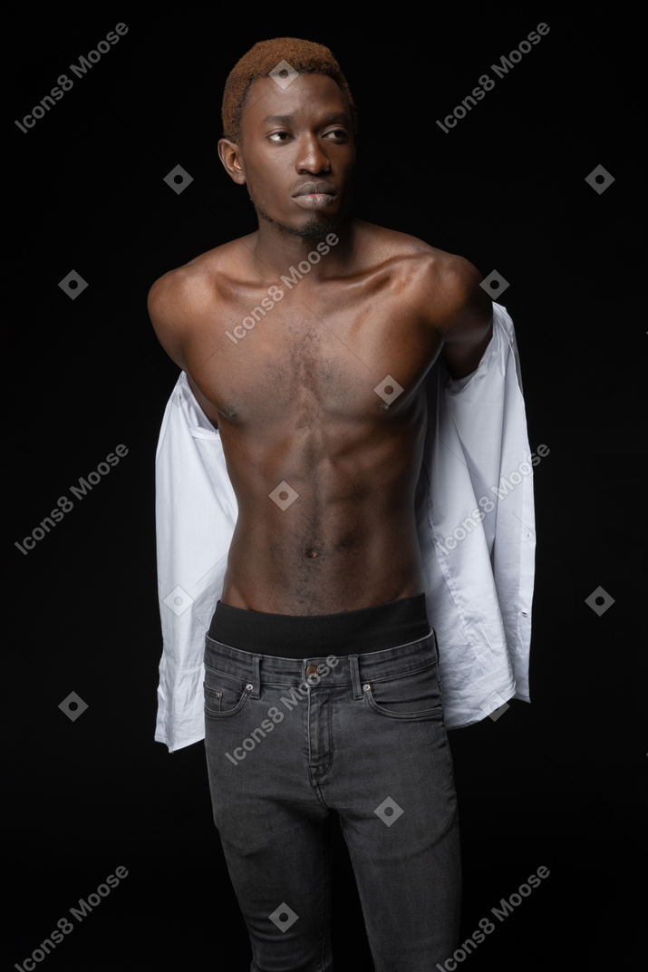 A muscular young male putting on a shirt in the dark