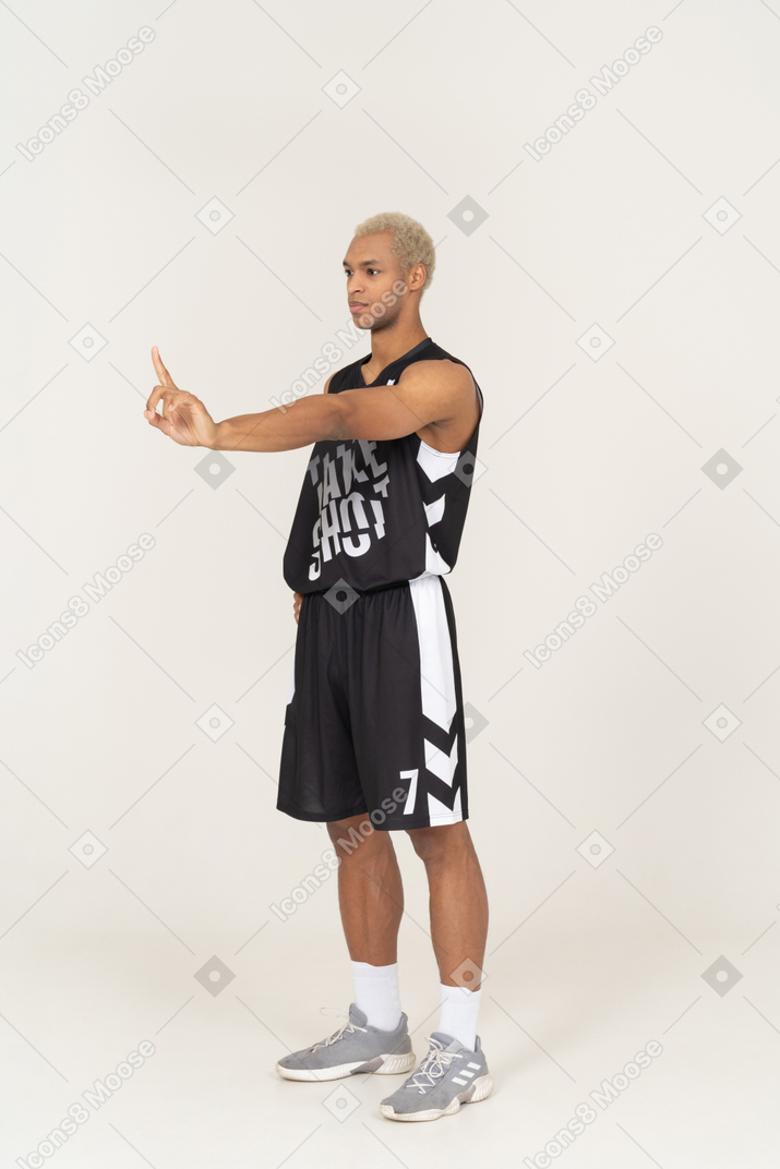 Vista de tres cuartos de un joven jugador de baloncesto masculino apuntando con el dedo hacia arriba