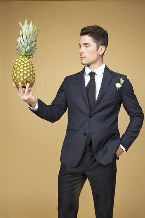 Groom in black suit holding a pineapple and like complimenting it