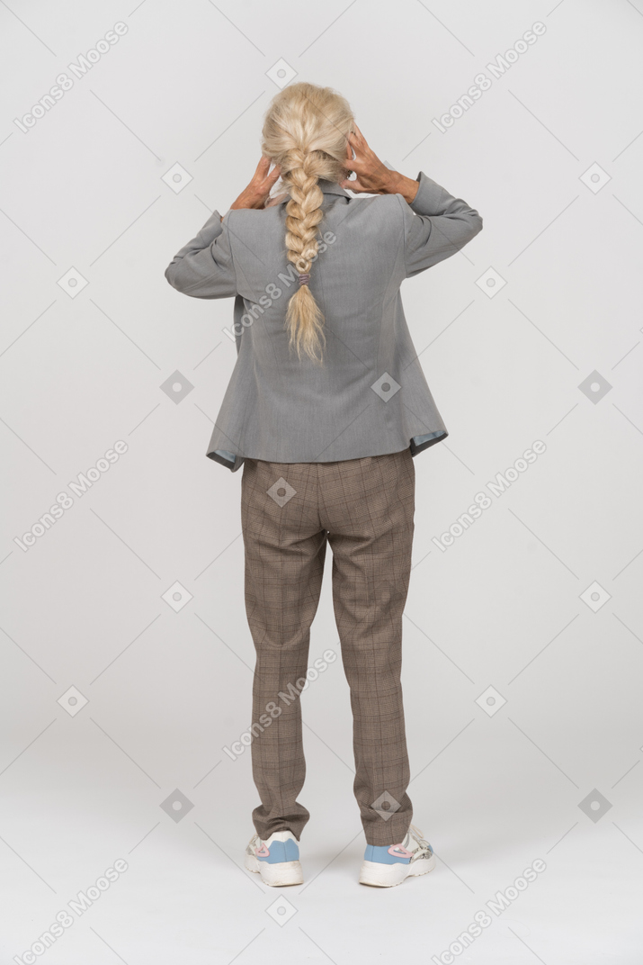 Vista posterior de una anciana en traje cubriendo las orejas con las manos