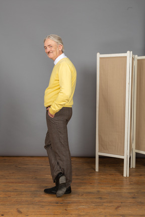 Side view of a smiling old man putting hand in pocket while looking at camera