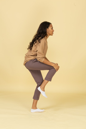 Vista lateral de una mujer joven de piel oscura tocando su rodilla lastimada