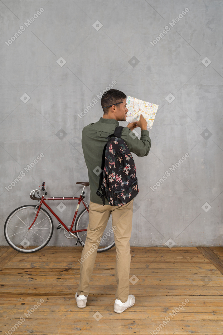 Rückansicht eines mannes mit rucksack und karte, der nach dem weg fragt