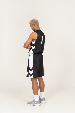 Vista posteriore di tre quarti di un giovane giocatore di basket maschile ritirato che incrocia le braccia