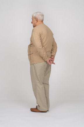 Side view of an old man in casual clothes standing with hands behind back