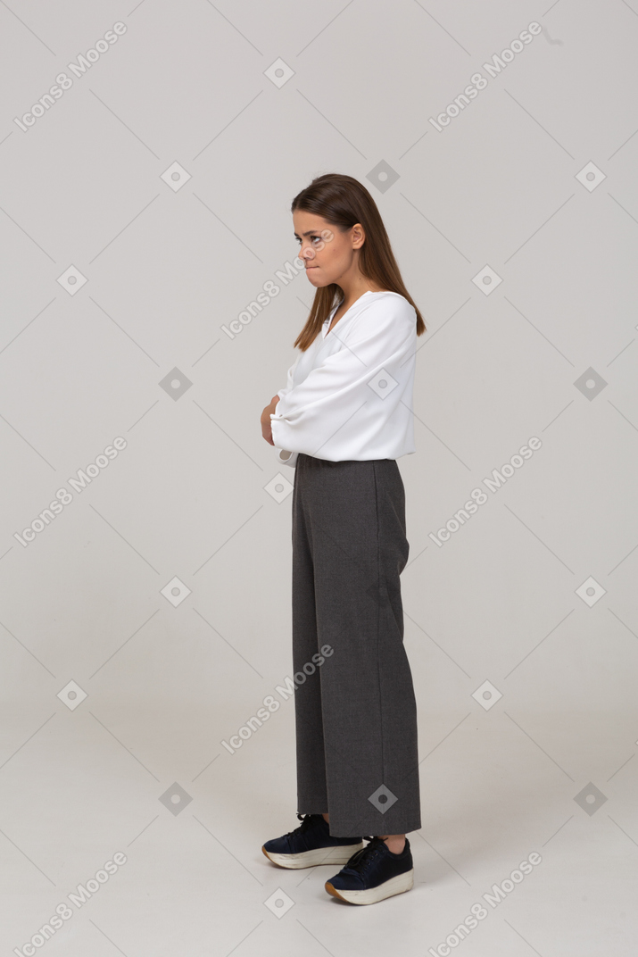 Vista de três quartos de uma jovem descontente com roupas de escritório, cruzando os braços