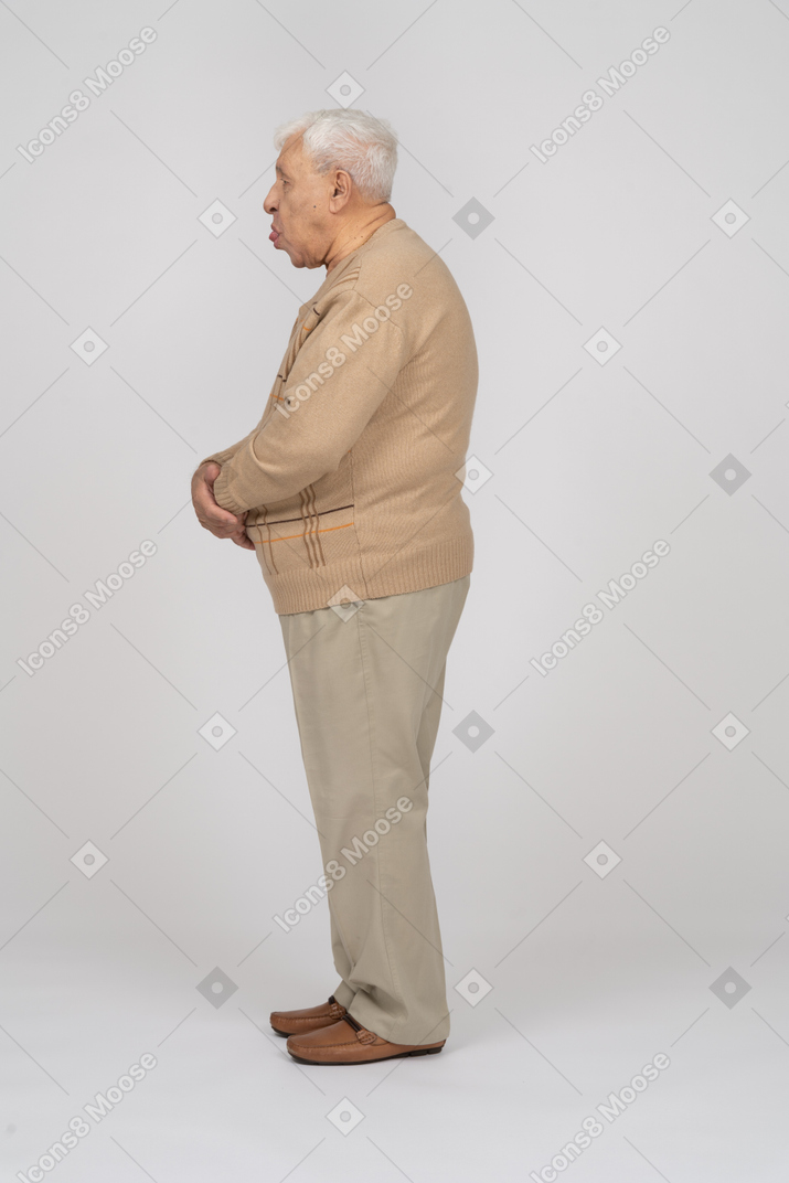 Вид сбоку на старика в повседневной одежде, корчащего рожи