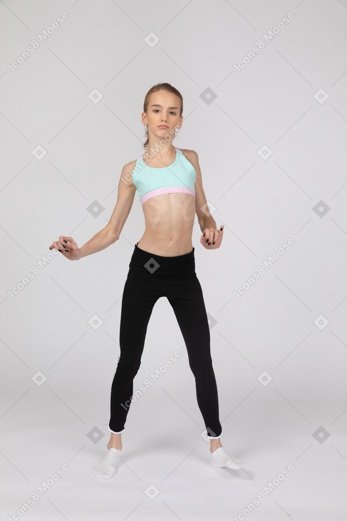 Front view of a teen girl in sportswear raising hands and her leg while dancing