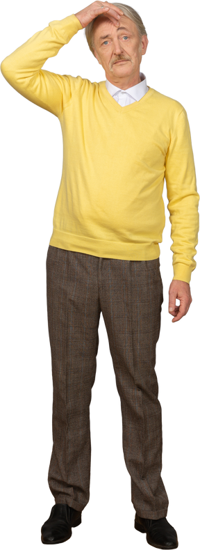 Front view of a confused old man touching head and wearing a yellow pullover