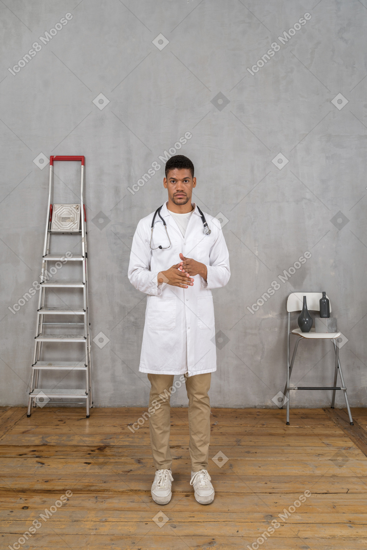 Вид спереди молодого врача, стоящего в комнате с лестницей и стулом