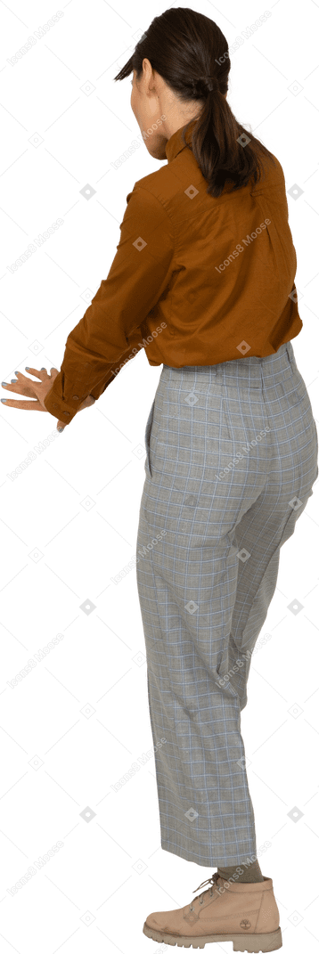 Vista posterior de tres cuartos de una joven mujer asiática en calzones y blusa extendiendo las manos