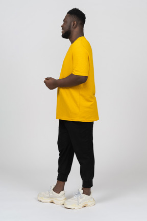 Vista laterale di un giovane uomo dalla pelle scura con una maglietta gialla in piedi immobile