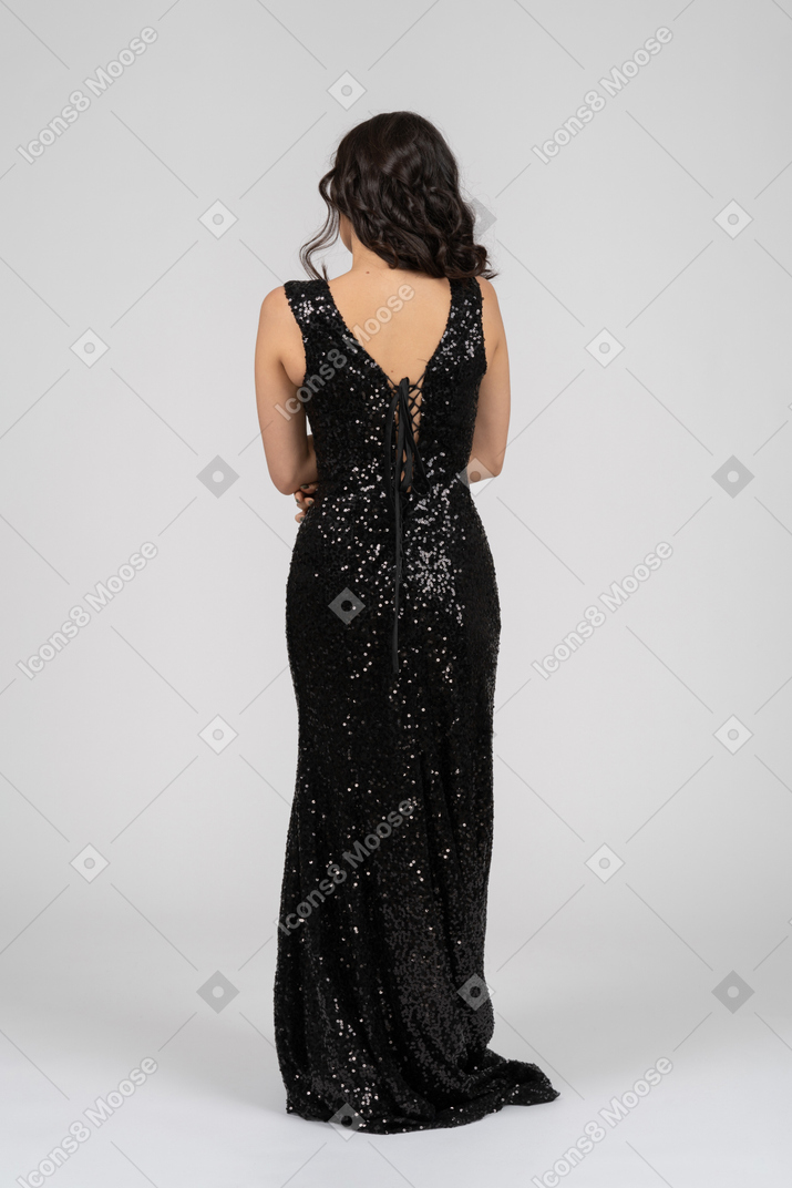 Woman in black evening dress standing back to camera with her arms crossed above