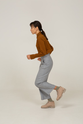 Vista lateral de uma jovem mulher asiática correndo de calça e blusa