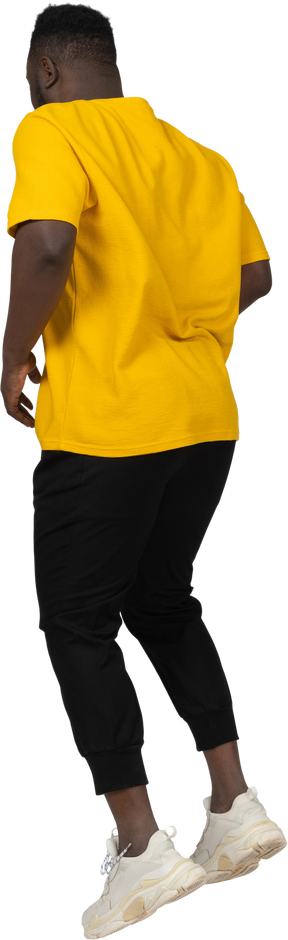 Vista posteriore di tre quarti di un giovane uomo dalla pelle scura che salta in maglietta gialla