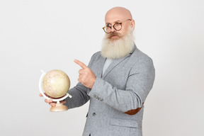 Strenger schauender alter professor, der globus hält und etwas zeigt