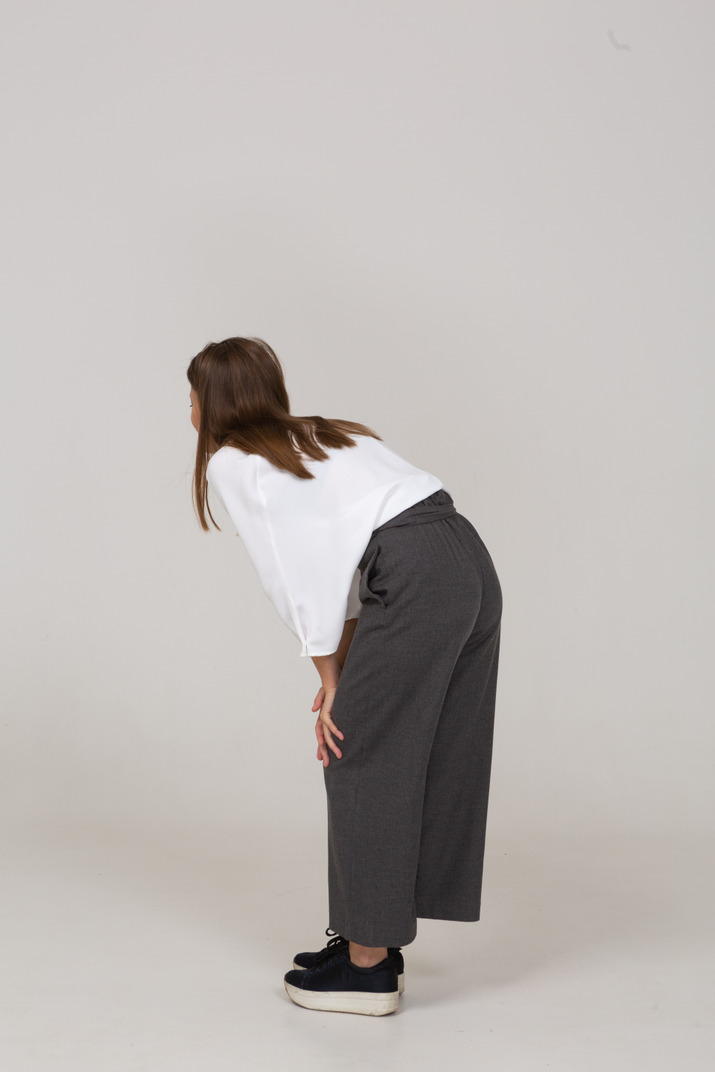 Three-quarter back view of a young lady in office clothing bending down & touching knee