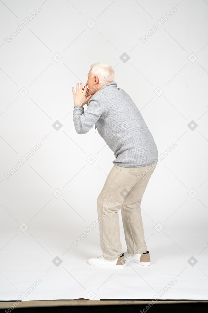 Vista posteriore di un uomo con le ginocchia piegate che si tiene per mano vicino alla bocca e urla