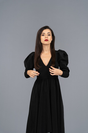 Vista frontale di una giovane donna seria che adegua il suo vestito nero