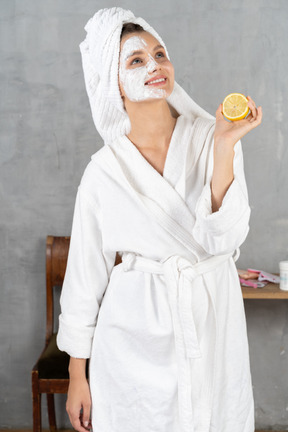 Mujer joven sonriente en bata de baño sosteniendo un limón