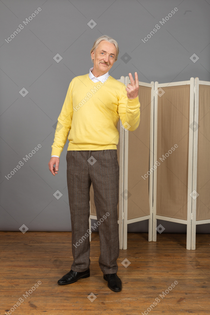 Vista frontal de un anciano mostrando el signo de la paz.