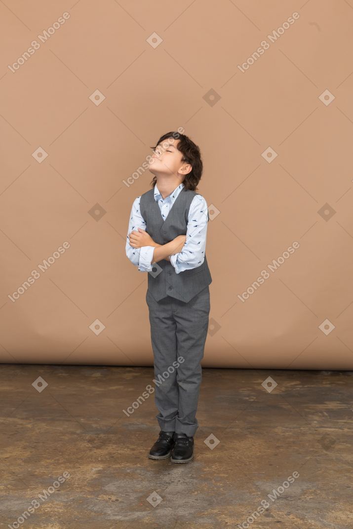 一个穿着灰色西装的男孩交叉双臂站立的正面图