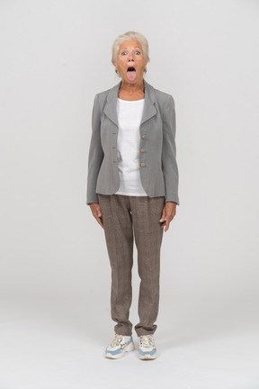 Vista frontal de una anciana en traje mirando a la cámara y mostrando la lengua