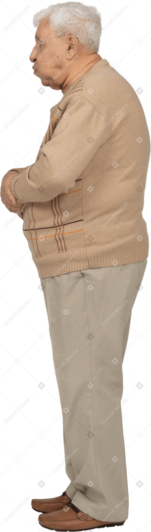 Vista lateral de un anciano con ropa informal de pie con los brazos cruzados y lanzando un beso
