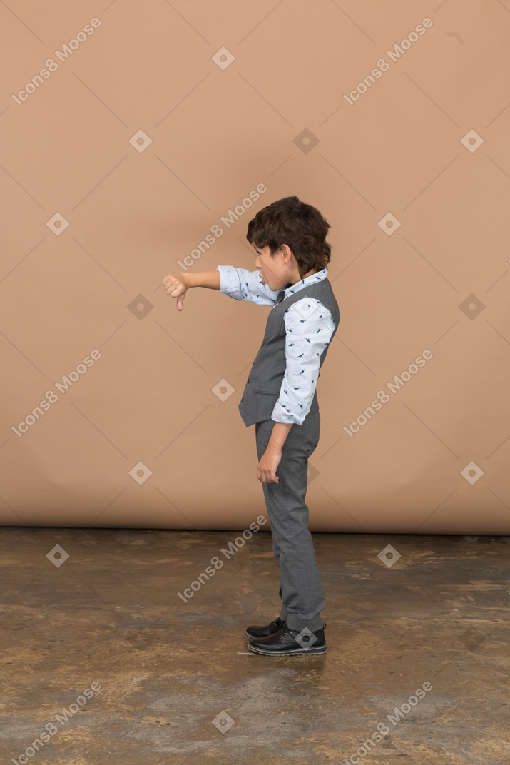 Vista lateral de um menino de terno cinza, mostrando o polegar para baixo