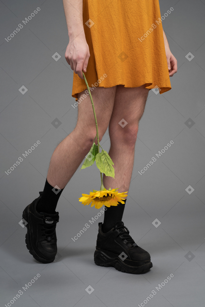 Foto recortada de uma pessoa de vestido laranja segurando um girassol