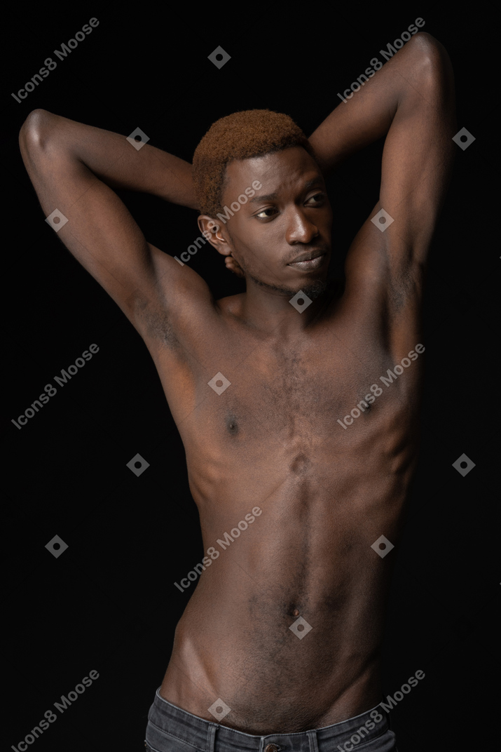 Macho africano musculoso levantando las manos sobre un fondo oscuro
