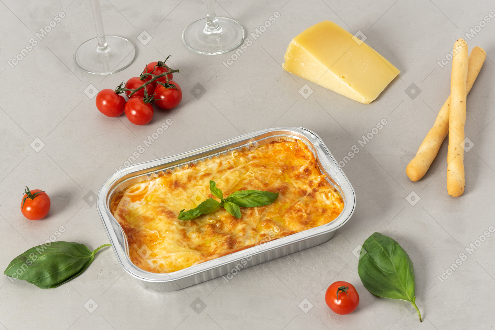Piece of lasagna, cheese, cherry tomatoes, grissini and glasses 