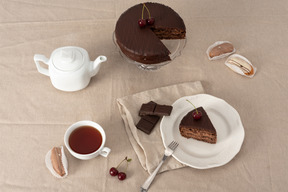 Chocolate cake on cake stand, teapot, cup of tea and piece of cake on the plate