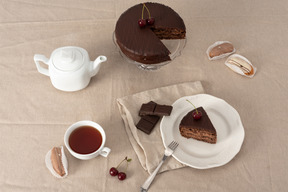 Gâteau au chocolat sur le support de gâteau, théière, tasse de thé et morceau de gâteau sur la plaque