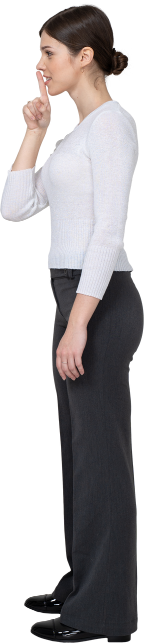 Side view of a young woman in office clothing showing silence gesture