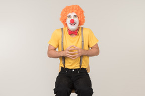 Smiling male clown in red wig sitting on the chair