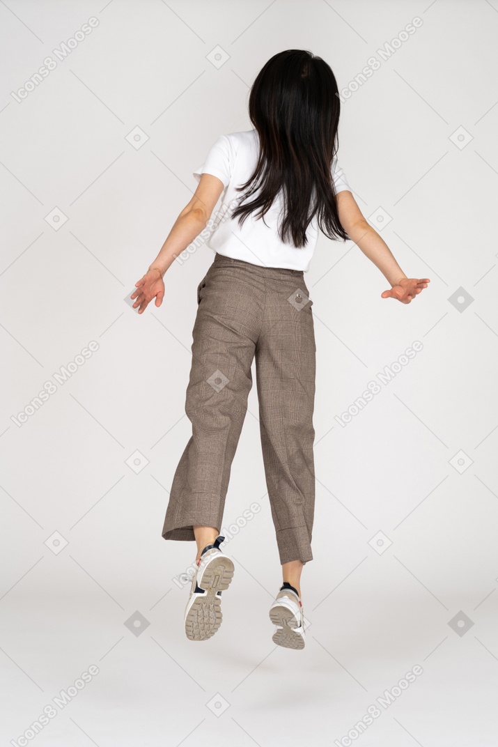 Vista de trás de uma jovem saltitante de calça e camiseta estendendo as mãos