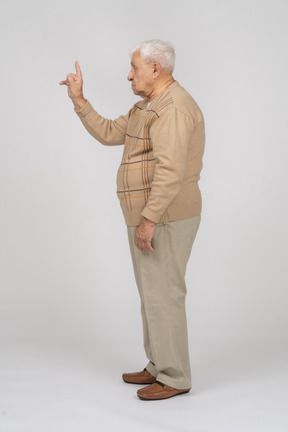 Vista lateral de un anciano con ropa informal apuntando hacia arriba con un dedo
