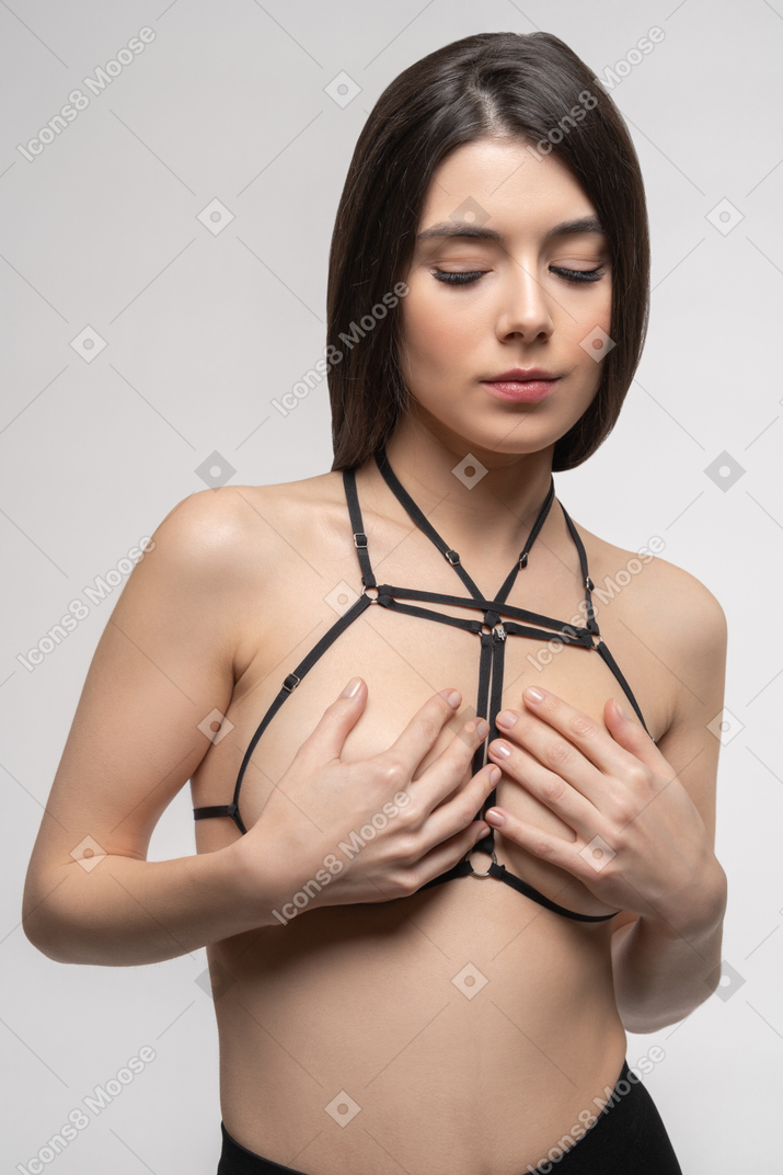 Front view of sexy young woman in harness covering breast with