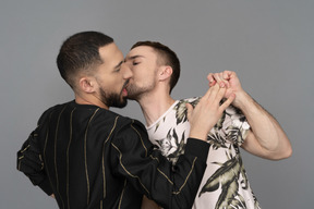 Young caucasian man leaning into his partner and holding his hand in attempt to kiss him