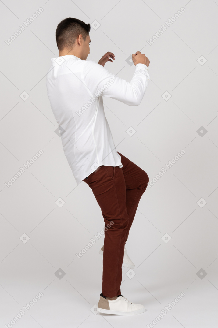 Dreiviertel-rückansicht eines jungen latino-mannes, der auf einem bein steht und wie überrascht die hände hebt