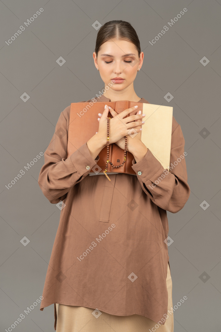 Woman with closed eyes holding book to chest