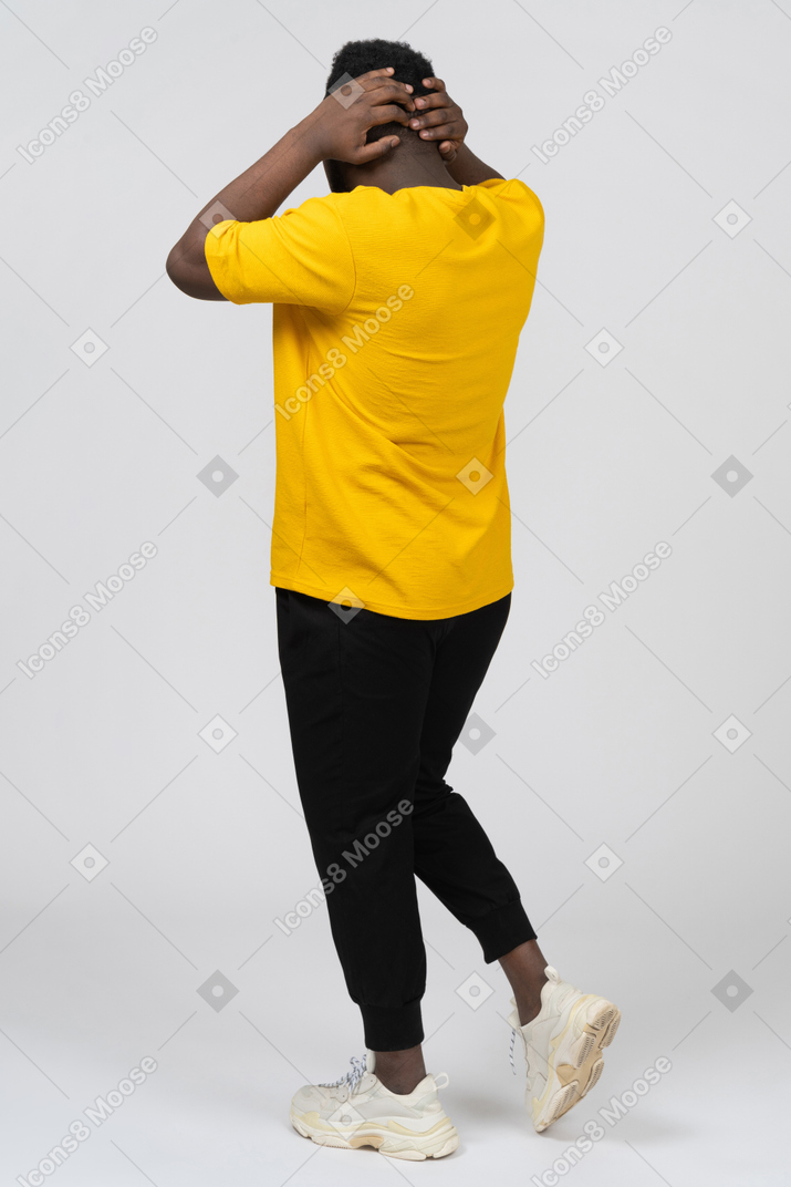 Three-quarter back view of a walking young dark-skinned man in yellow t-shirt touching head
